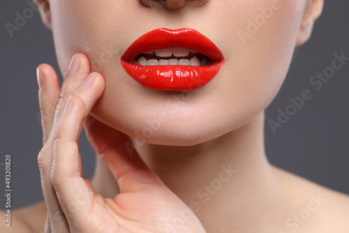 Young woman with beautiful red lips on grey background, closeup