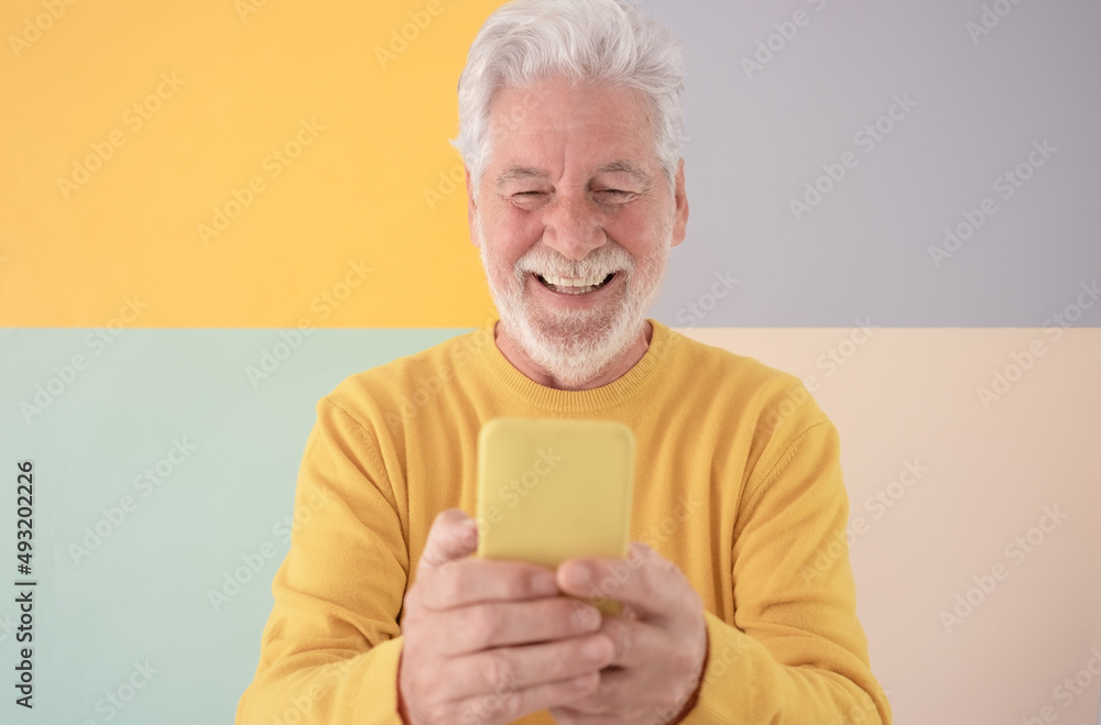 Old handsome bearded senior man wearing yellow sweater holding mobile phone in video chat standing over isolated colorful background. Elderly man enjoying tech and social Old handsome bearded senior man wearing yellow sweater holding mobile phone in video chat standing over isolated colorful background. Elderly man enjoying tech and social