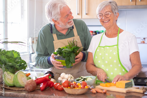 Attractive senior couple preparing vegetables together in the home kitchen laughing amused. Caucasian elderly people enjoying healthy eating