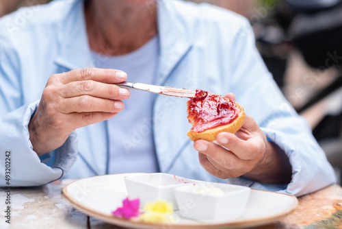 Mature caucasian woman sitting at an outdoor table spreads strawberry jam on toast. Healthy and tasty breakfast or snack