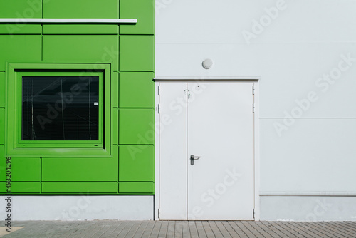 Exterior of modern industrial building, closed white door and window. Emergency exit or entrance, frontal view on sunny day outdoors