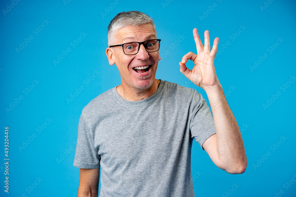 Happy positive handsome old man shows Ok sign over blue background Happy positive handsome old man shows Ok sign over blue background