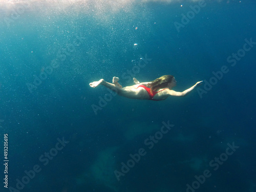 Young woman swims underwater in blue sea