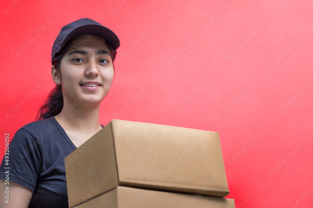 Smiling Young Delivery Woman Holding Cardboard Box Against Color Background Smiling Young Delivery Woman Holding Cardboard Box Against Color Background