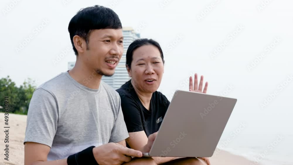 2 Asian brothers A woman and a man with a mustache sitting on the beach with laptops at the beach. Video call with friends and relax on vacation at the seaside on a bright day 2 Asian brothers A woman and a man with a mustache sitting on the beach with laptops at the beach. Video call with friends and relax on vacation at the seaside on a bright day