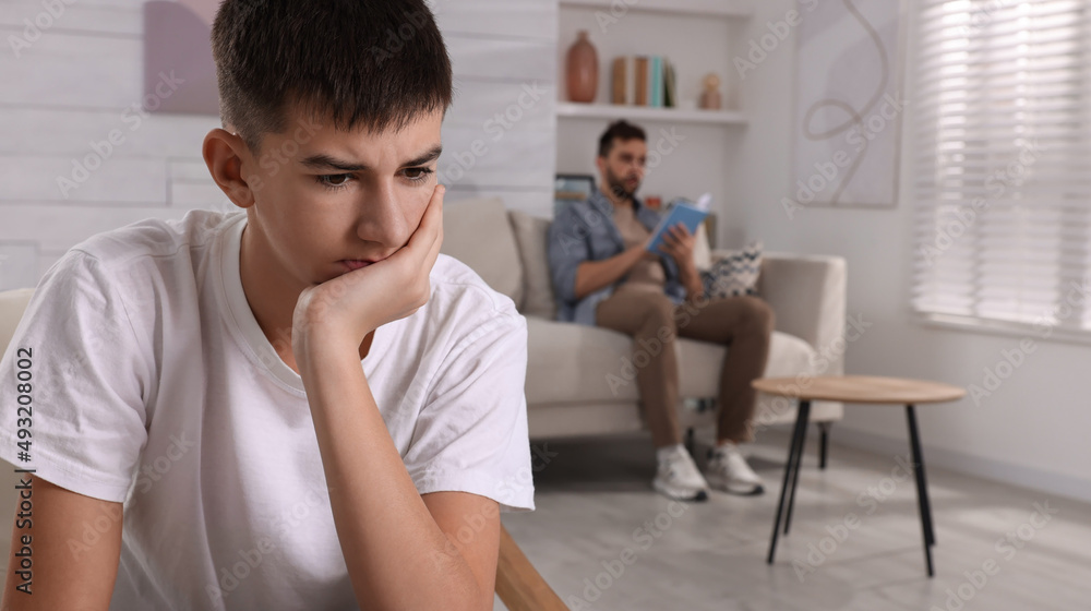Unhappy teenage boy suffering from lack of father's attention in living room. Problems at home