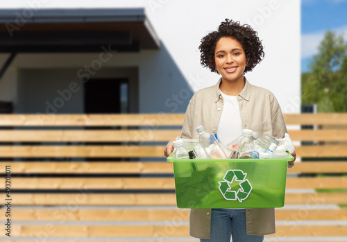 waste sorting and sustainability concept - smiling young african american woman holding plastic box with trash over living house background