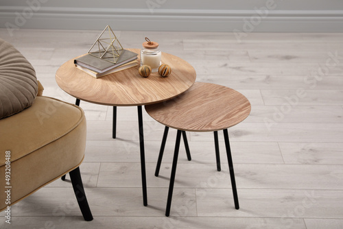 Wooden nesting tables with books and decor near armchair indoors photo