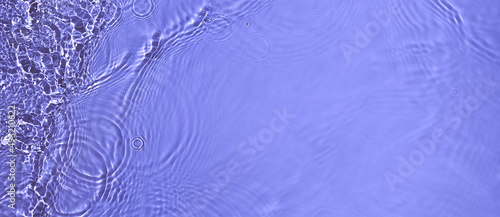 Transparent purple clear water surface texture with ripples and splashes. Abstract summer banner background Water waves in sunlight, copy space, top view. Cosmetic moisturizer micellar toner emulsion