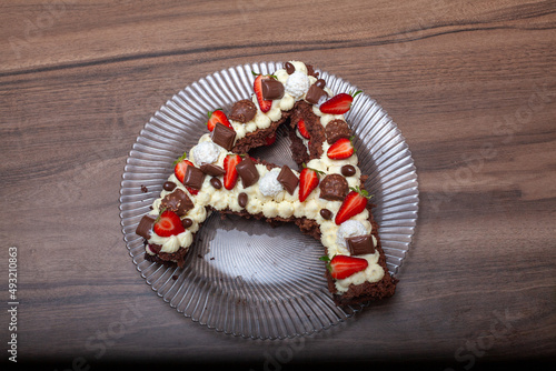 Cake in the shape of the letter A. Birthday cake with strawberry and chocolates. Cake with whipped cream and wooden background. 