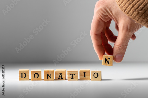 charity and financial help concept - close up of hand making donation word with wooden toy blocks