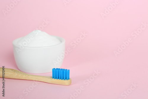 Bamboo toothbrush and bowl with baking soda on pink background. Space for text