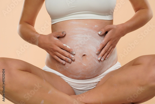 Cropped view of pregnant woman applying cosmetic cream on her belly to avoid stretch marks