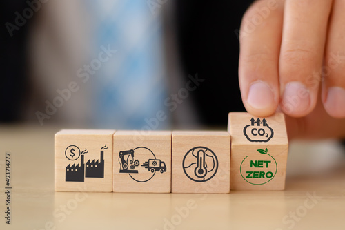 Net zero target and carbon neutral. Green business concept. Climate changing problems solving goals..Businessman flips wooden cubes from pollution sources to net zero target icon on smart background.