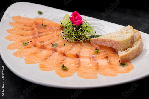 Salmon carpaccio with herbs, on a plate, on a dark background