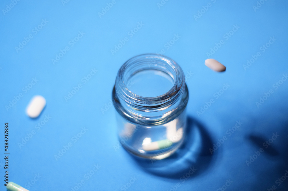 Glass container and pills on blue background. Glass container and pills on blue background.