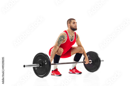 Full length portrait of man in red sportswear exercising with a weight isolated on white background. Sport, weightlifting, power, achievements concept