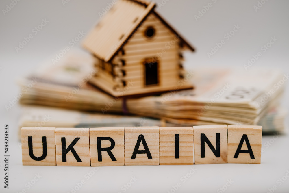 Napis Ukraina na tle domku stojącego na stosie banknotów - obrazy, fototapety, plakaty 
