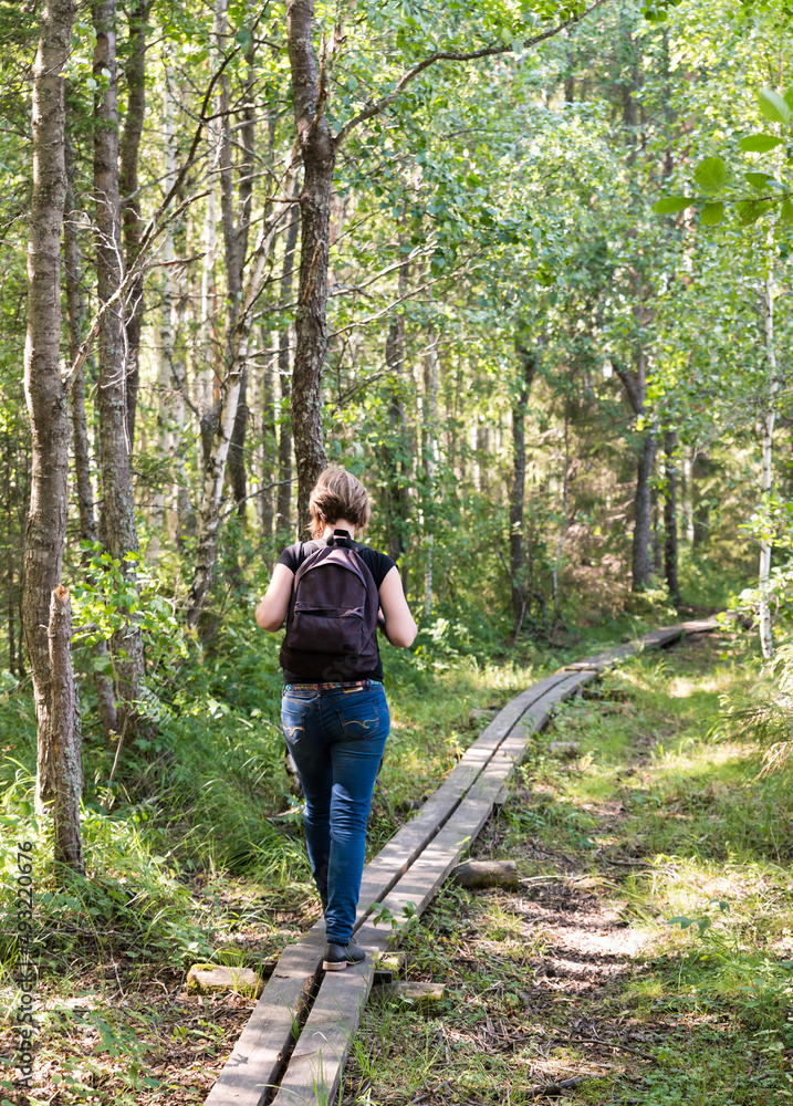 Young healthy woman with backpack walking over a wooden path in the Florarna Naturreservat Young healthy woman with backpack walking over a wooden path in the Florarna Naturreservat