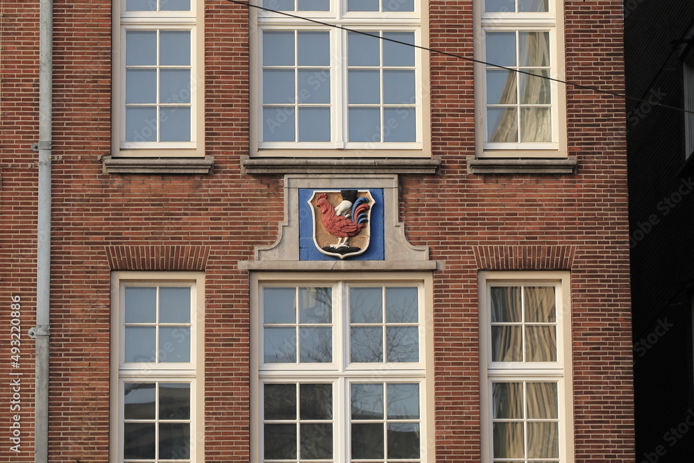 Amsterdam Damrak Street Brick Building Close Up with Stone Tablet Depicting a Hand Holding a Red Chicken, Netherlands Amsterdam Damrak Street Brick Building Close Up with Stone Tablet Depicting a Hand Holding a Red Chicken, Netherlands