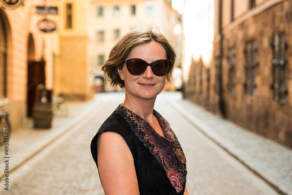 Portrait of a smiling thirty year old white woman with a black dress and sunglass in the Sunny Streets of Stockholm Old Town