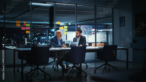 Businesspeople in Modern Office: Business Meeting of Two Managers. CEO and Operations Director Talk, Discuss, Brainstorm Corporate Strategy, Implementing Marketing and Financial Plans. Evening Time. © Gorodenkoff