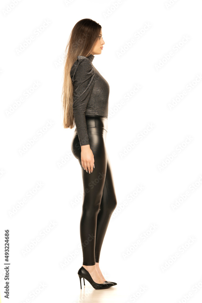 An attractive young woman posing in gray blouse and latex trousers. Fashion look on a white background. An attractive young woman posing in gray blouse and latex trousers. Fashion look on a white background.