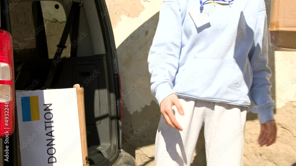 Two volunteer man and young woman being unloaded from the car boxes with donation food and drinks for the refugees people from Ukraine. Two volunteer man and young woman being unloaded from the car boxes with donation food and drinks for the refugees people from Ukraine.