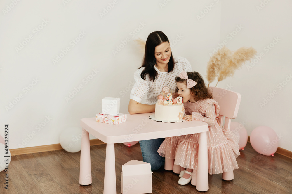 A young mother and her little daughter celebrate their birthday with a cake. A young mother and her little daughter celebrate their birthday with a cake.