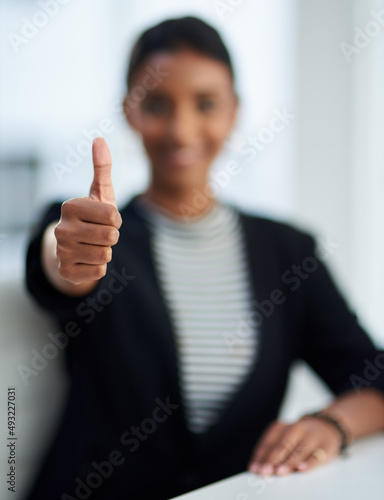 You get a thumbs up from me. Defocused shot of a young businesswoman posing with her thumbs up at work.