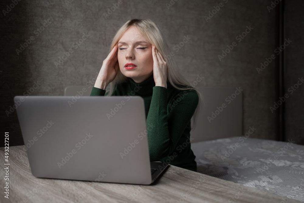 A sad and very tired blonde woman in a green golf is bored working at home with a laptop. Girl sitting at the table in a bad mood in the room. Online learning. Unsightly video conference. High quality A sad and very tired blonde woman in a green golf is bored working at home with a laptop. Girl sitting at the table in a bad mood in the room. Online learning. Unsightly video conference. High quality