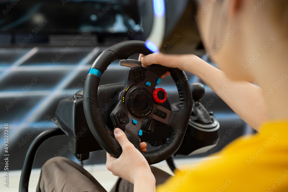 Close-up of the hands of a teenage boy in virtual reality glasses, who is holding the steering wheel and playing a computer game on the console.