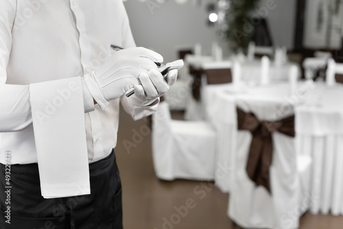 Waiter in a white shirt and bow tie writing down an order in a cafe, close up.
