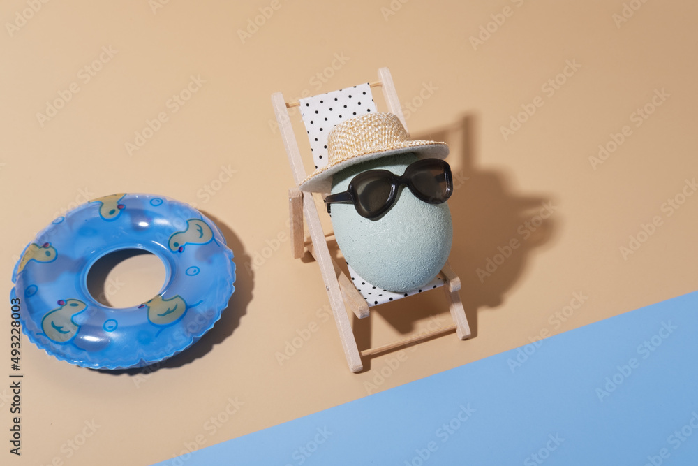 Naklejka premium A cheerful Easter composition with an egg in sunglasses lies on a sun lounger on the beach
