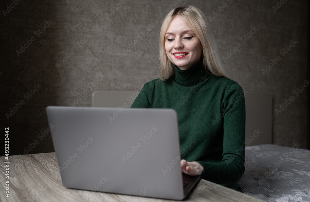 Happy smiling blonde girl in green golf joyfully works online at home with a laptop. Sits at the table in a good mood in the room. High quality photo Happy smiling blonde girl in green golf joyfully works online at home with a laptop. Sits at the table in a good mood in the room. High quality photo