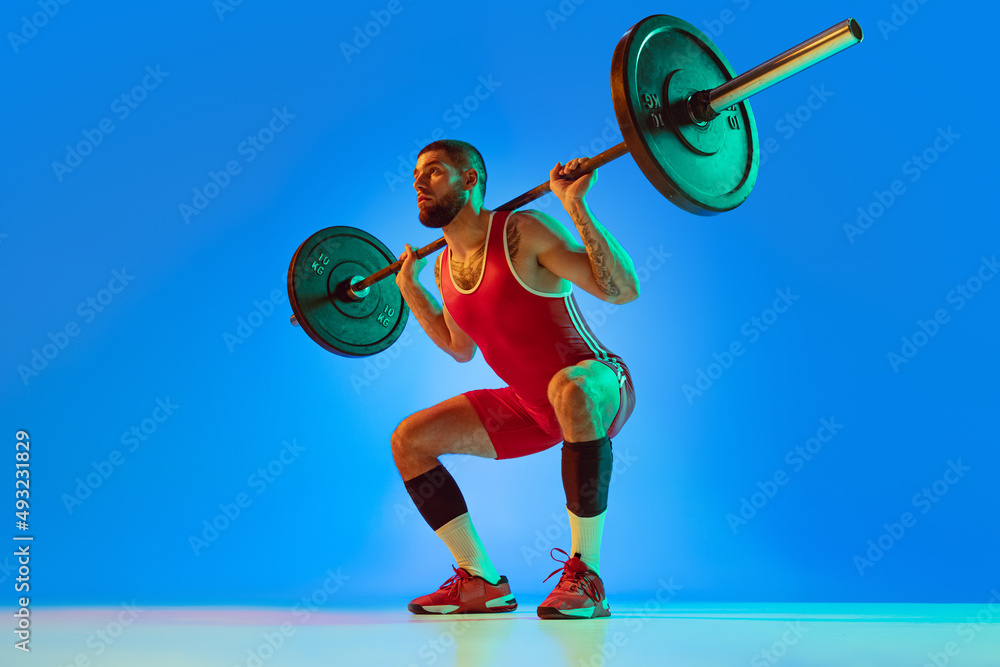 Studio shot of young man in red sportswear exercising with barbell isolated  blue background in neon. Sport, weightlifting, power, achievements concept  Stock Photo | Adobe Stock