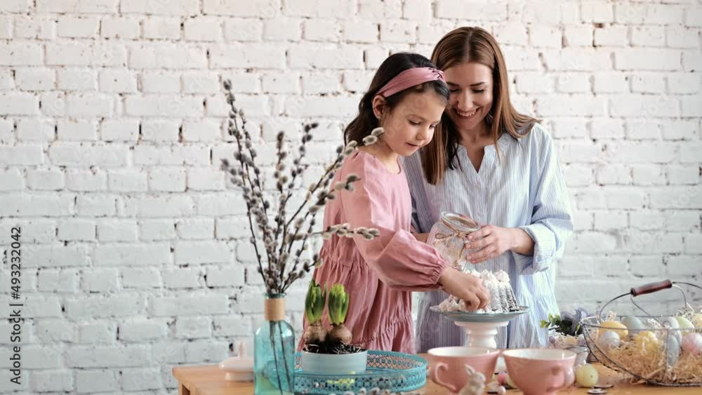 Cute little kid daughter helping mom adding flour to eggs preparing dough for cookies together in modern kitchen, happy mother teaching small child girl learning cooking baking cake pastry at home Cute little kid daughter helping mom adding flour to eggs preparing dough for cookies together in modern kitchen, happy mother teaching small child girl learning cooking baking cake pastry at home
