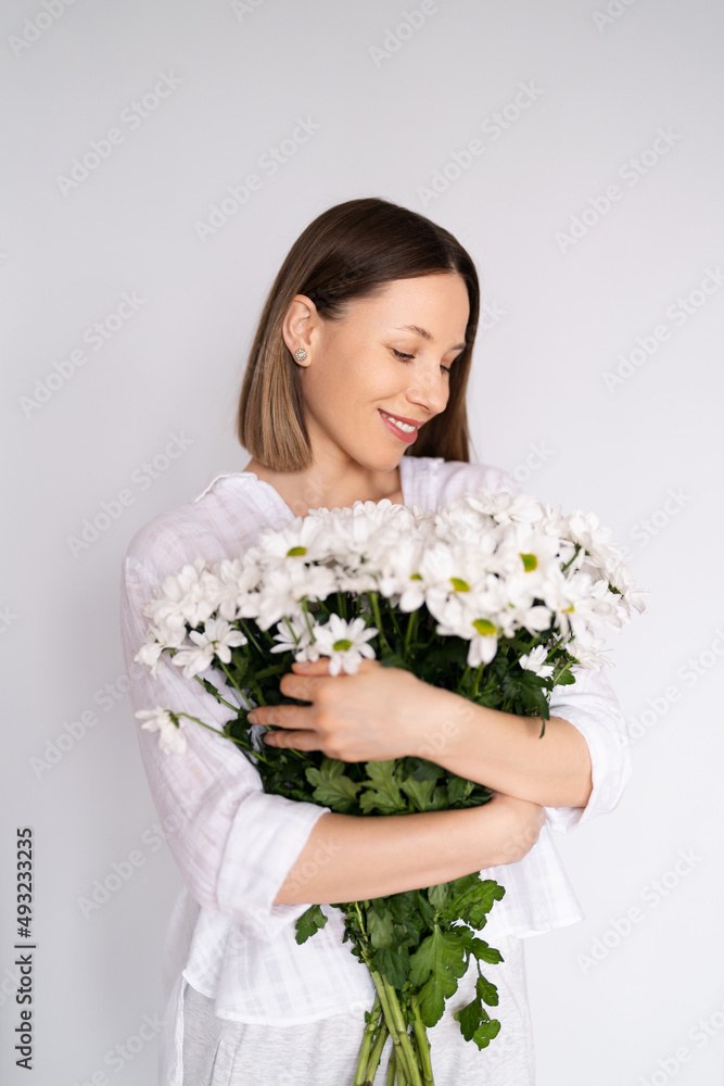 Young beautiful cute sweet lovely smiling woman with hold a bouquet of white fresh flowers on white wall background