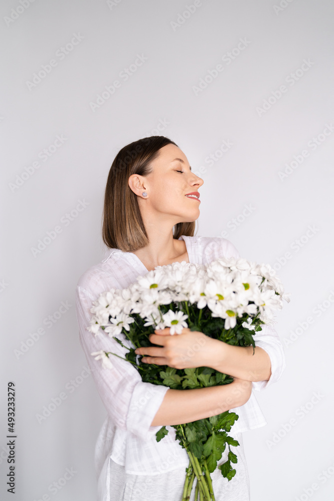 Young beautiful cute sweet lovely smiling woman with hold a bouquet of white fresh flowers on white wall background