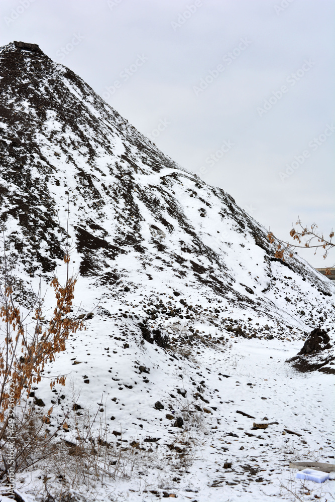 Bright, colorful high mountains, peaks, steep hills are located along the road and covered with light white snow in winter. A very interesting and bewitching landscape against a gray-white sky. 