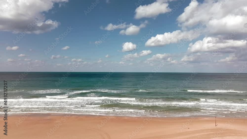 Waves breaking on a clear sandy beach with cloudy blue sky in the background.
Waves breaking on a clear sandy beach with cloudy blue sky in the background.