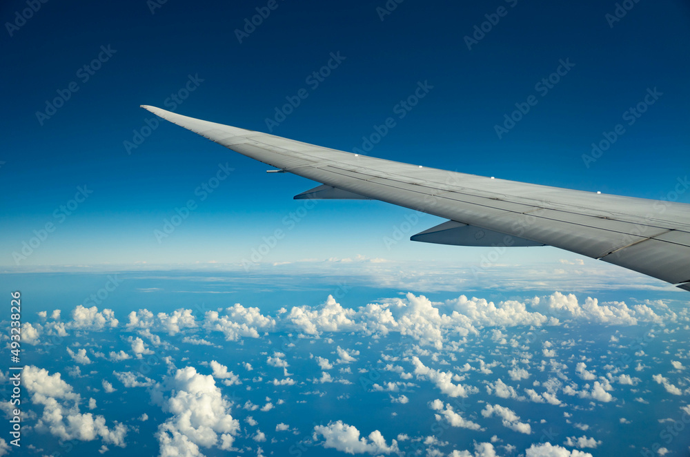 Wing of an airplane flying over morning clouds. View on cloud and blue sky through the airplane window. Wing of an airplane flying over morning clouds. View on cloud and blue sky through the airplane window.