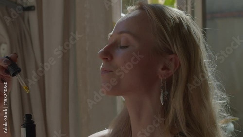 Pretty caucasian girl is doing self-healing with natural therapy organic ingredients essence of flowers or herbs. Puts several drops under her tongue with the help of a pipette. 4k high-quality video
