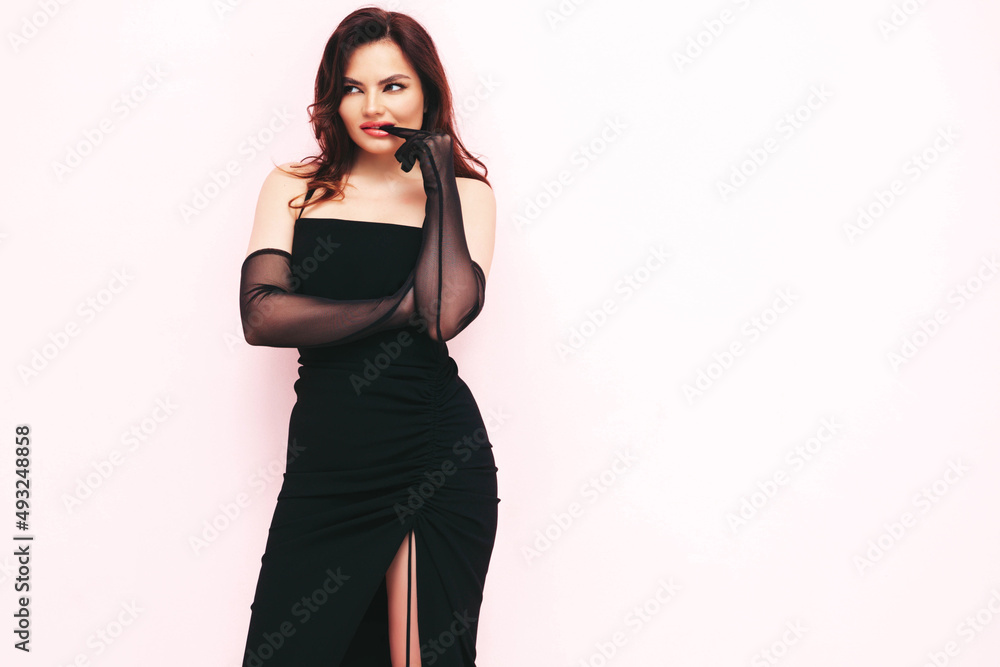 High fashion portrait of young beautiful brunette woman wearing nice trendy black evening dress and biting her gloves. Sexy fashion model posing in studio. Fashionable female isolated on pink High fashion portrait of young beautiful brunette woman wearing nice trendy black evening dress and biting her gloves. Sexy fashion model posing in studio. Fashionable female isolated on pink