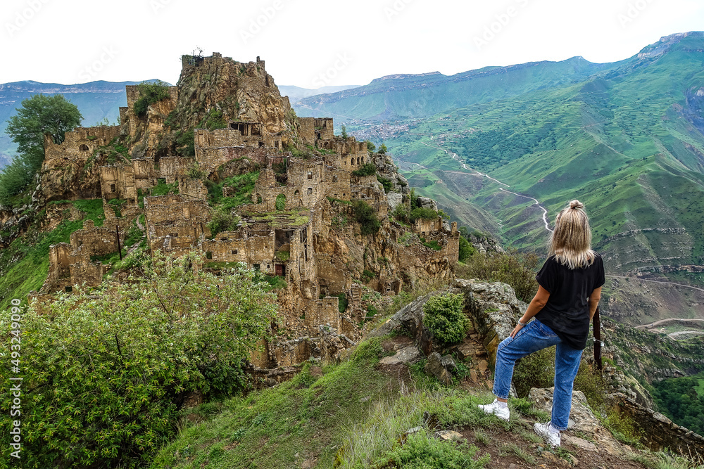 A girl on the background of Gamsutl village in the Caucasus mountains, on top of a cliff. Dagestan Russia June 2021