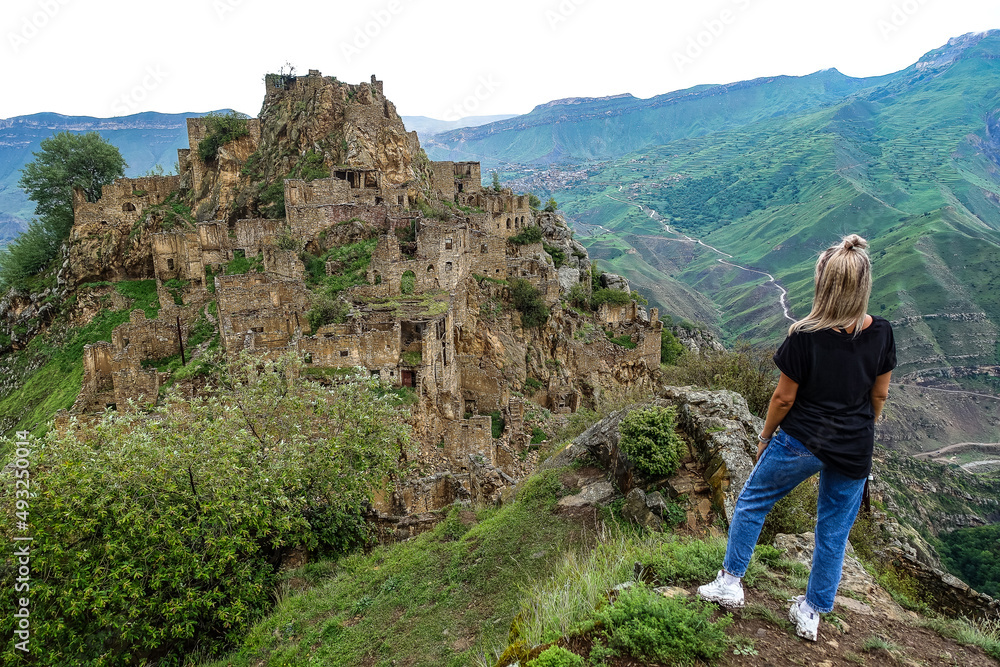 A girl on the background of Gamsutl village in the Caucasus mountains, on top of a cliff. Dagestan Russia June 2021 A girl on the background of Gamsutl village in the Caucasus mountains, on top of a cliff. Dagestan Russia June 2021