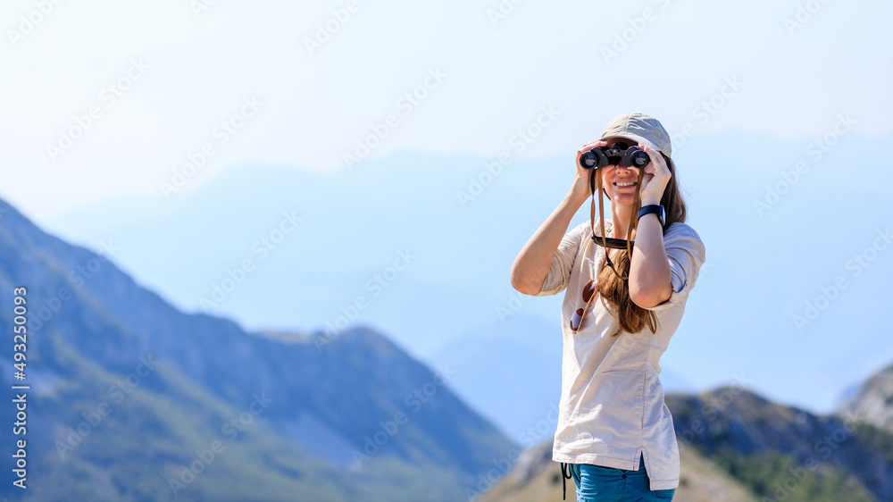 Young woman watching mountain landscape through binoculars at the view spot on tourist trail