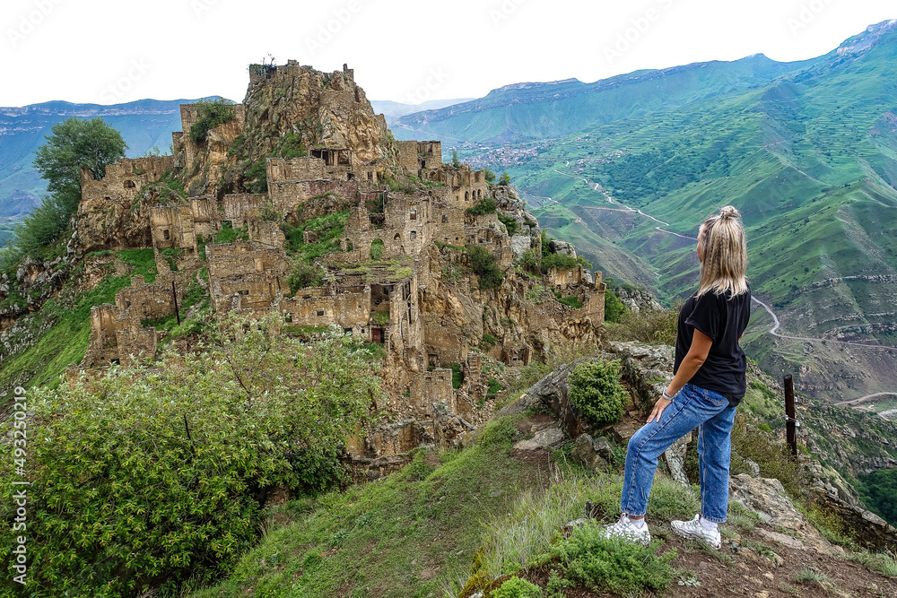Fototapeta premium A girl on the background of Gamsutl village in the Caucasus mountains, on top of a cliff. Dagestan Russia June 2021
