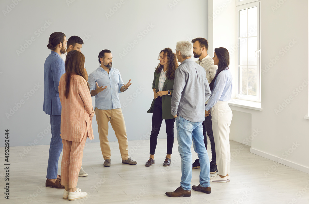 People talking during informal meeting. Creative business team communicates and discusses ideas for future business project standing in still empty office. Concept of starting your own business. People talking during informal meeting. Creative business team communicates and discusses ideas for future business project standing in still empty office. Concept of starting your own business.