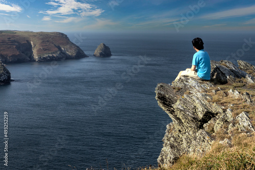 Man sitting on a rocky ledge looking towards the coast in Boscastle, Cornwall, UK. photo